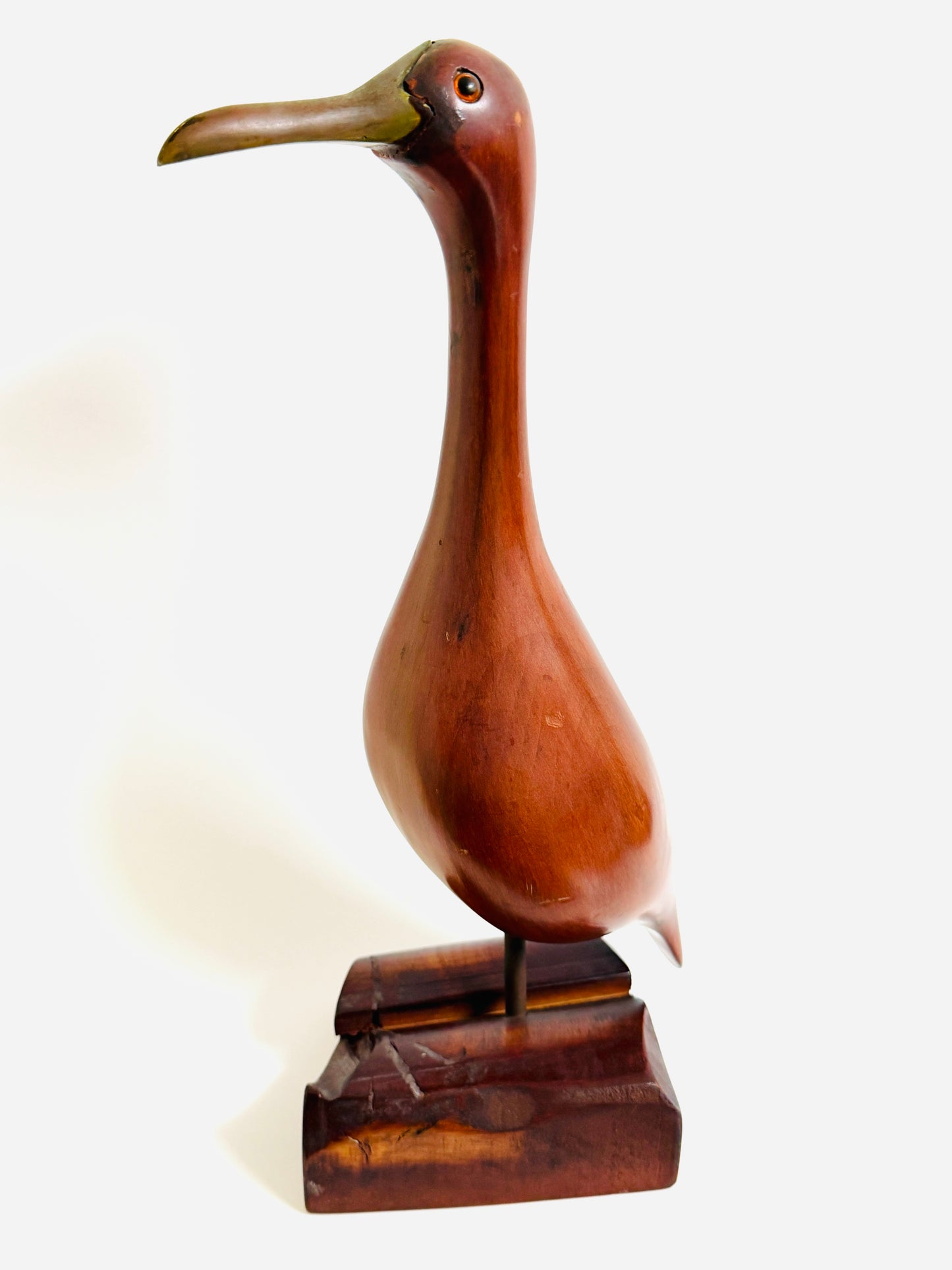 A carved wooden bird sculpture with a long neck and beak, mounted on a dark wooden base 