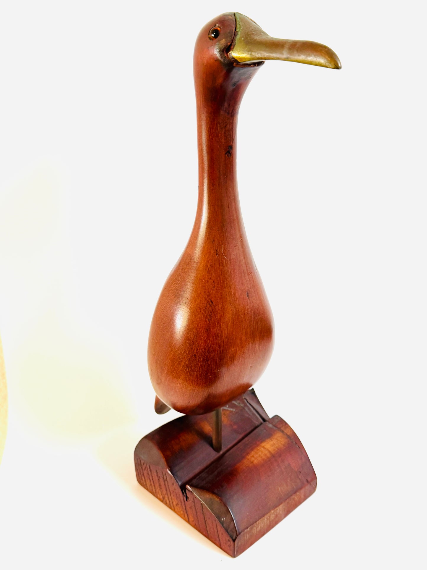 A carved wooden duck figurine with a polished reddish-brown body and a metallic gold-toned beak, standing on a matching wooden base 