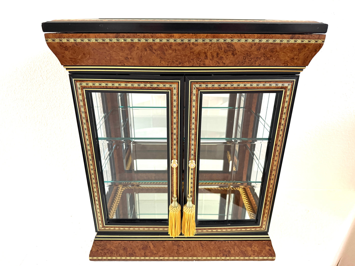A vintage-style display cabinet with two glass doors, featuring a rich brown burl wood veneer, black trim, gold geometric inlay, and gold tassels on the door handles made in Italy 