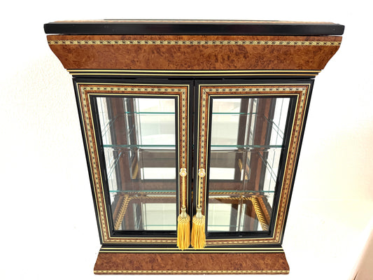A vintage-style display cabinet with two glass doors, featuring a rich brown burl wood veneer, black trim, gold geometric inlay, and gold tassels on the door handles made in Italy 