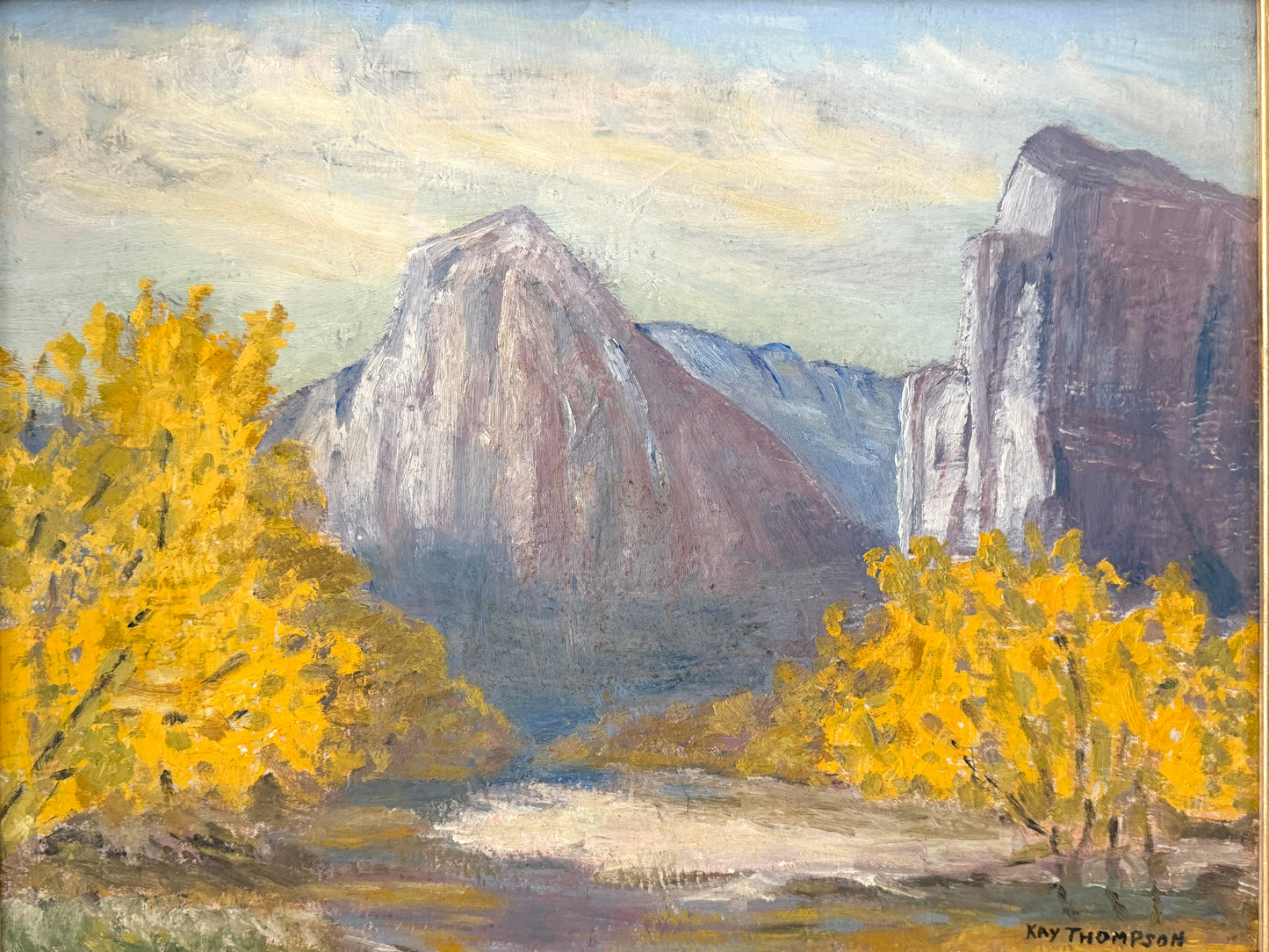 An oil painting of a mountain landscape with bright yellow autumn trees in the foreground, featuring a large central rock formation and a river or path in the valley. Signed 'Kay Thompson' in the lower right corner.
