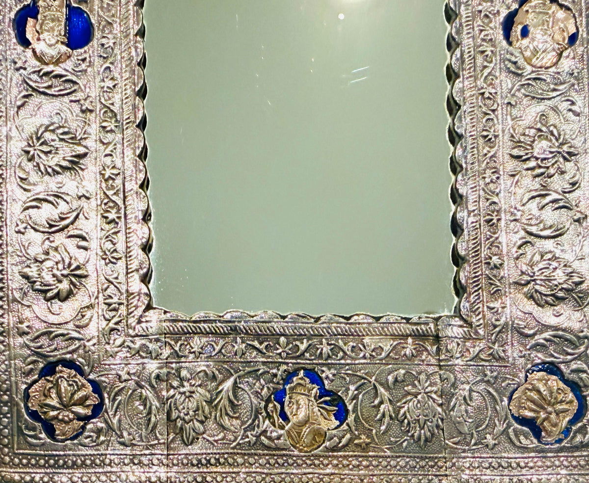 An ornate rectangular mirror with a highly detailed, hand-carved silver-toned frame featuring floral motifs and small blue and gold accents.