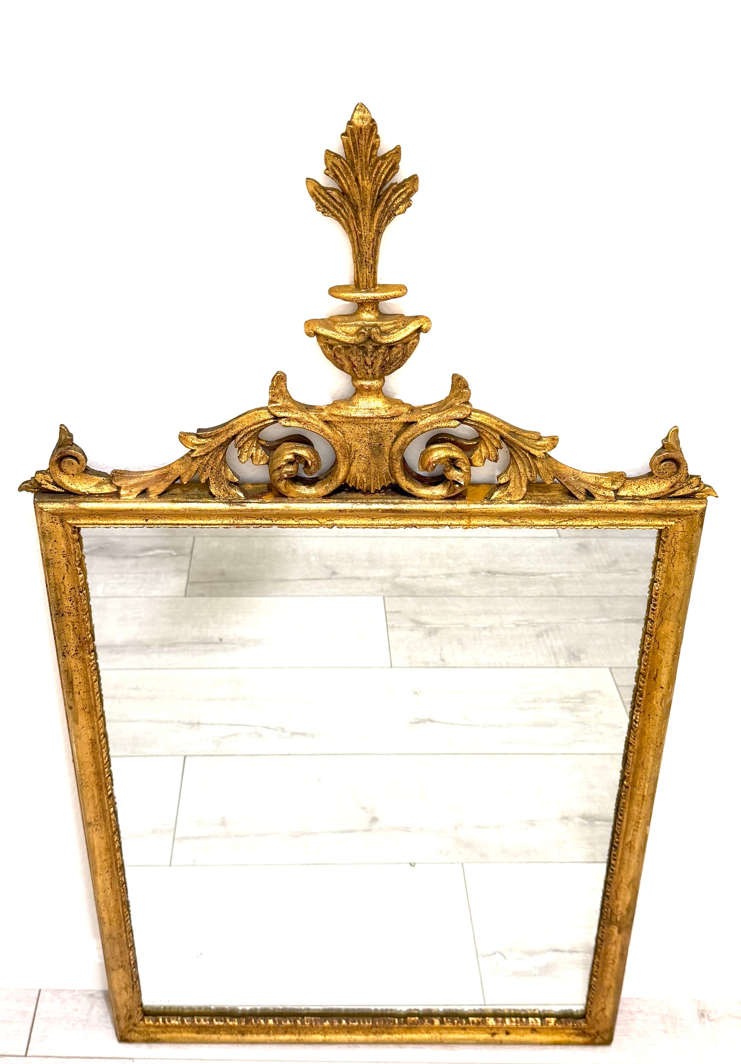 An ornate antique-style rectangular mirror with a gilded gold frame, featuring a decorative crest and acanthus leaf motif at the top.