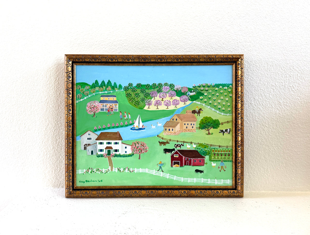 A framed folk art landscape painting depicting a rural scene with houses, barns, trees, fields, and a river Signed Kay Benham 06