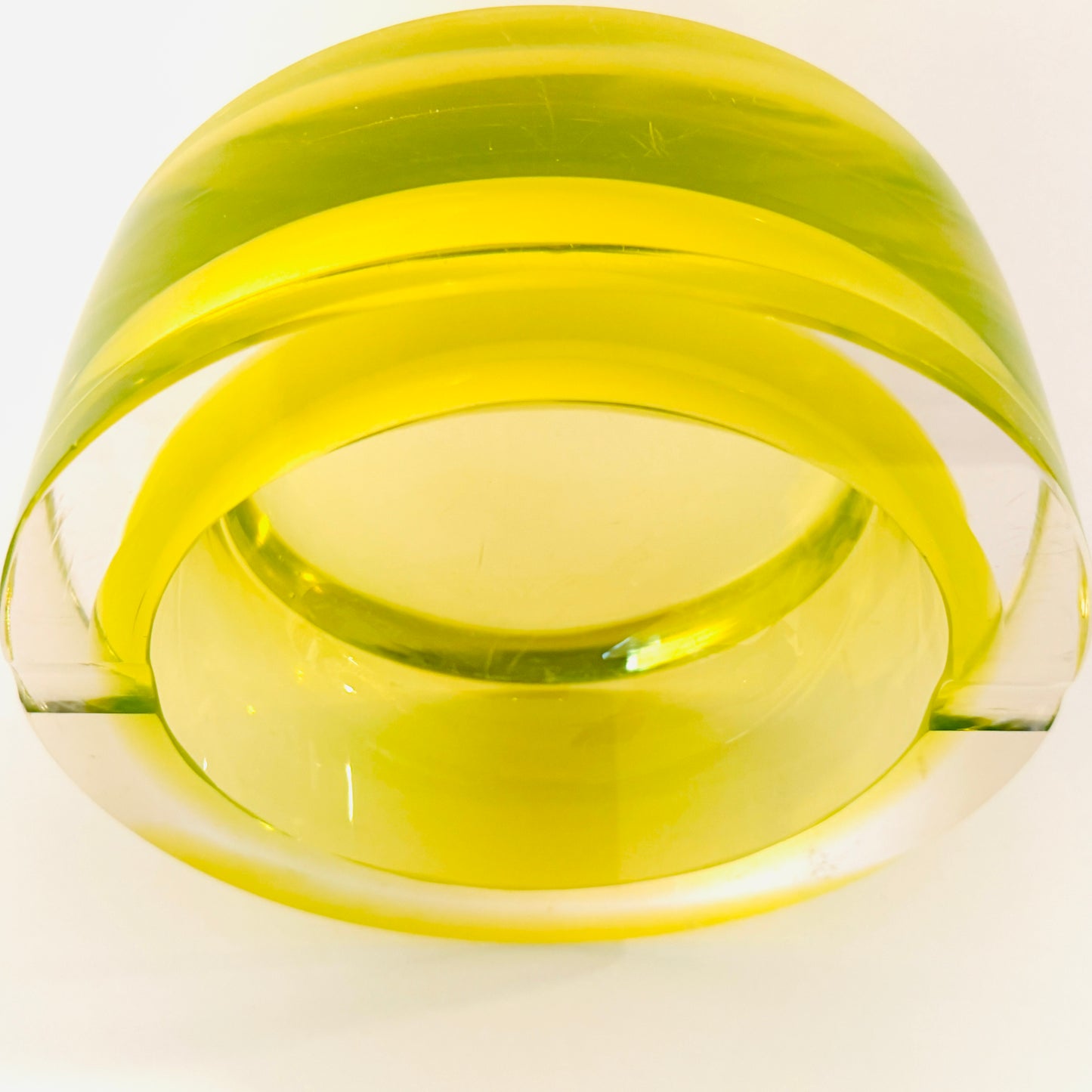 A translucent yellow-green glass bowl with a wide rim, photographed on a plain white background.