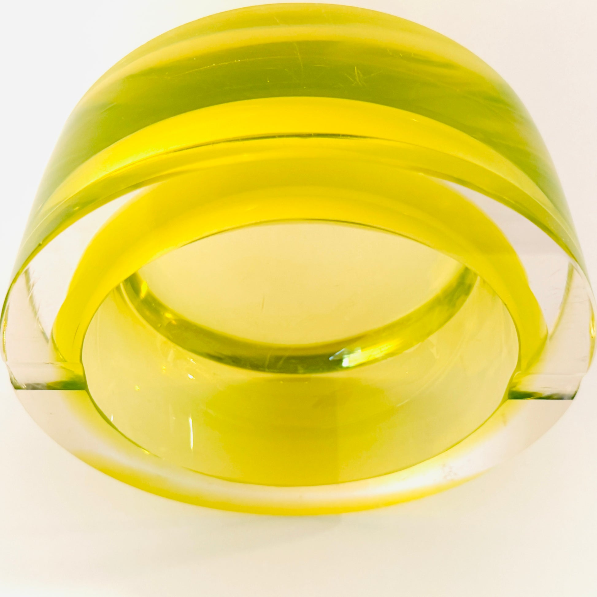 A translucent yellow-green glass bowl with a wide rim, photographed on a plain white background.