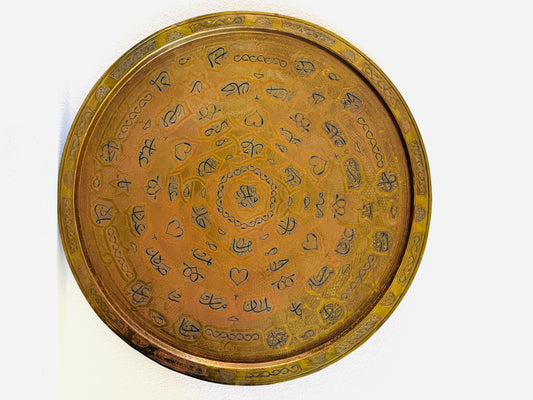 A round brass decorative tray with intricate engraved Arabic calligraphy and floral motifs