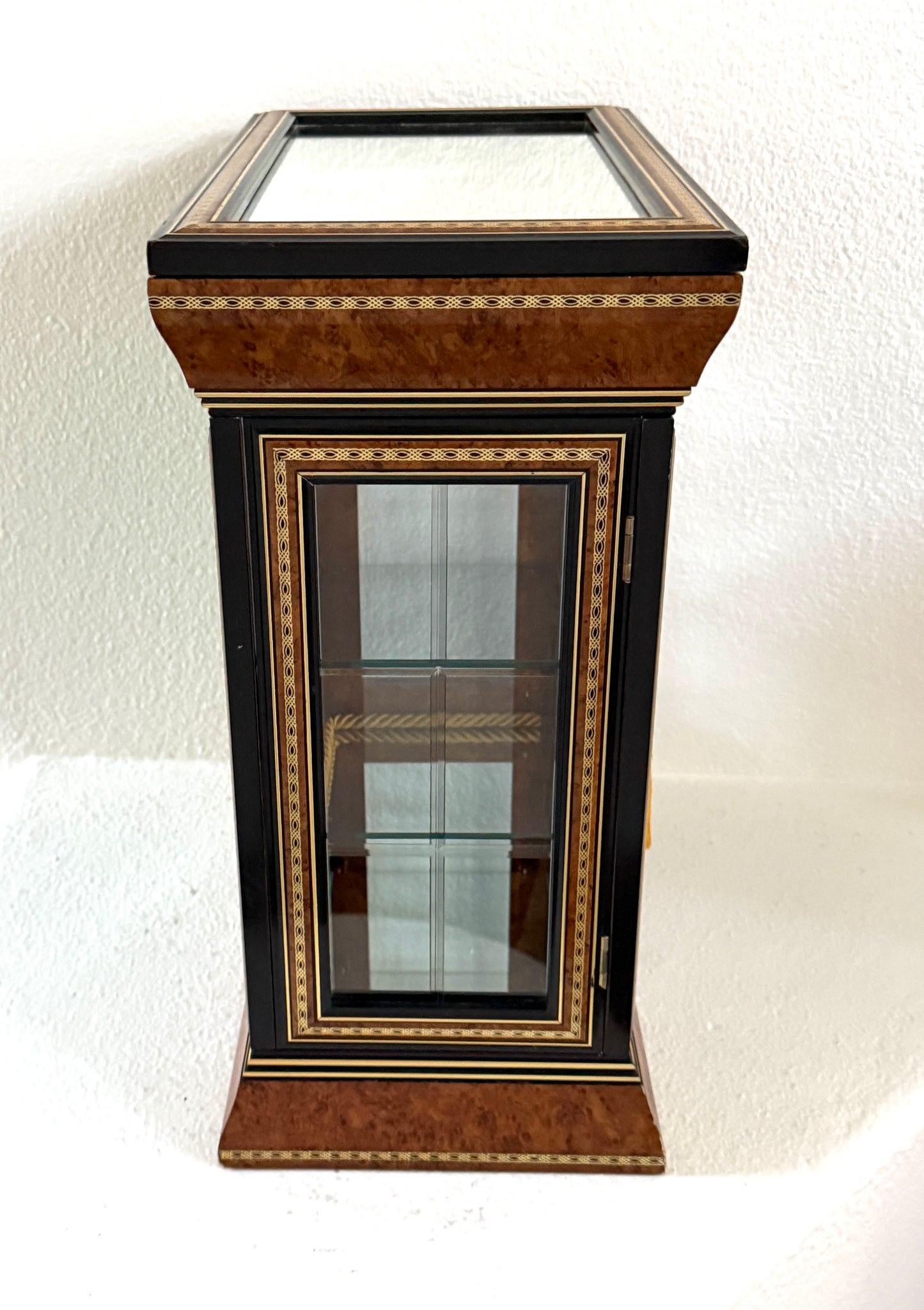 A vintage-style display cabinet with two glass doors, featuring a rich brown burl wood veneer, black trim, gold geometric inlay, and gold tassels on the door handles made in Italy