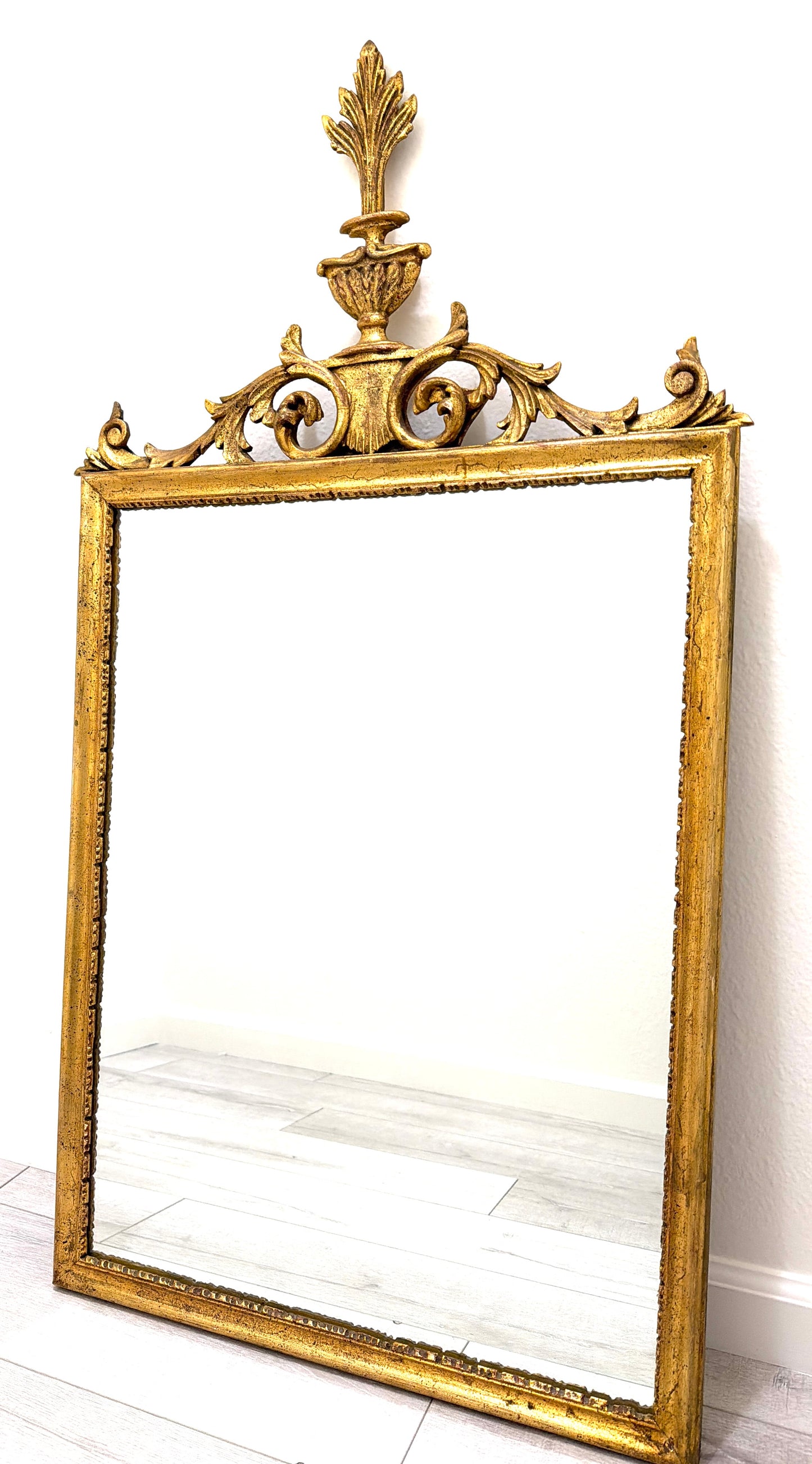An ornate gold-framed wall mirror with a decorative acanthus leaf crest and scrollwork top.