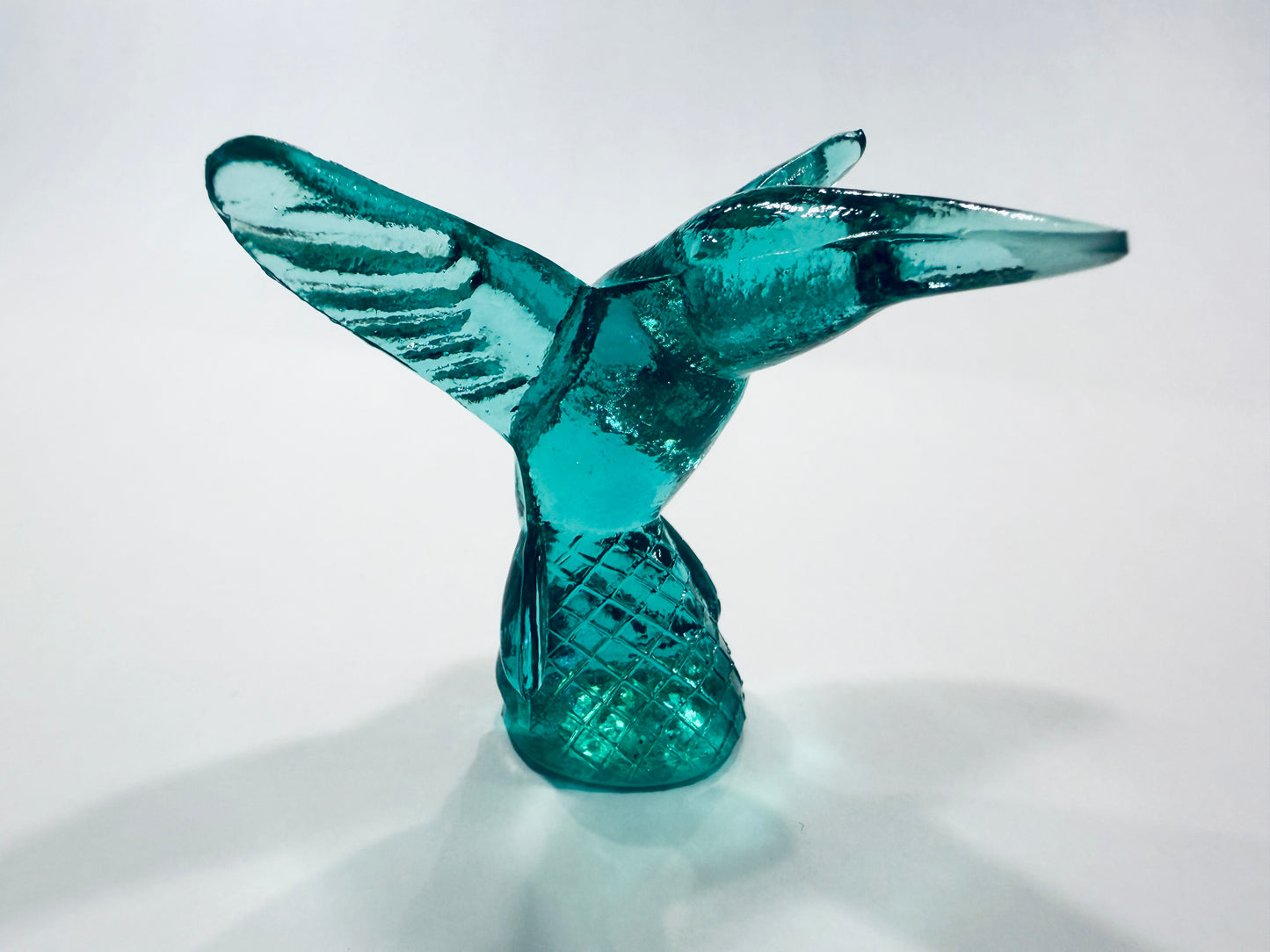 A translucent teal blue glass sculpture of a hummingbird in flight, standing on a textured base Made In Italy 