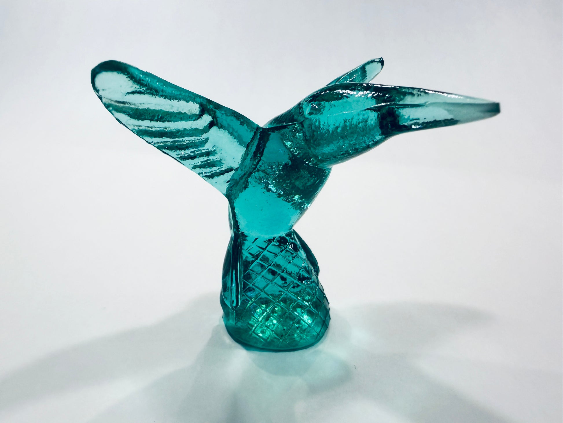 A translucent teal blue glass sculpture of a hummingbird in flight, standing on a textured base Made In Italy 