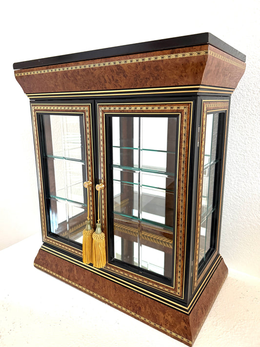 An ornate Art Deco style glass display cabinet with a rich brown burl wood veneer, black lacquered trim, gold geometric inlay, and gold tassels on the doors, Made in Italy 