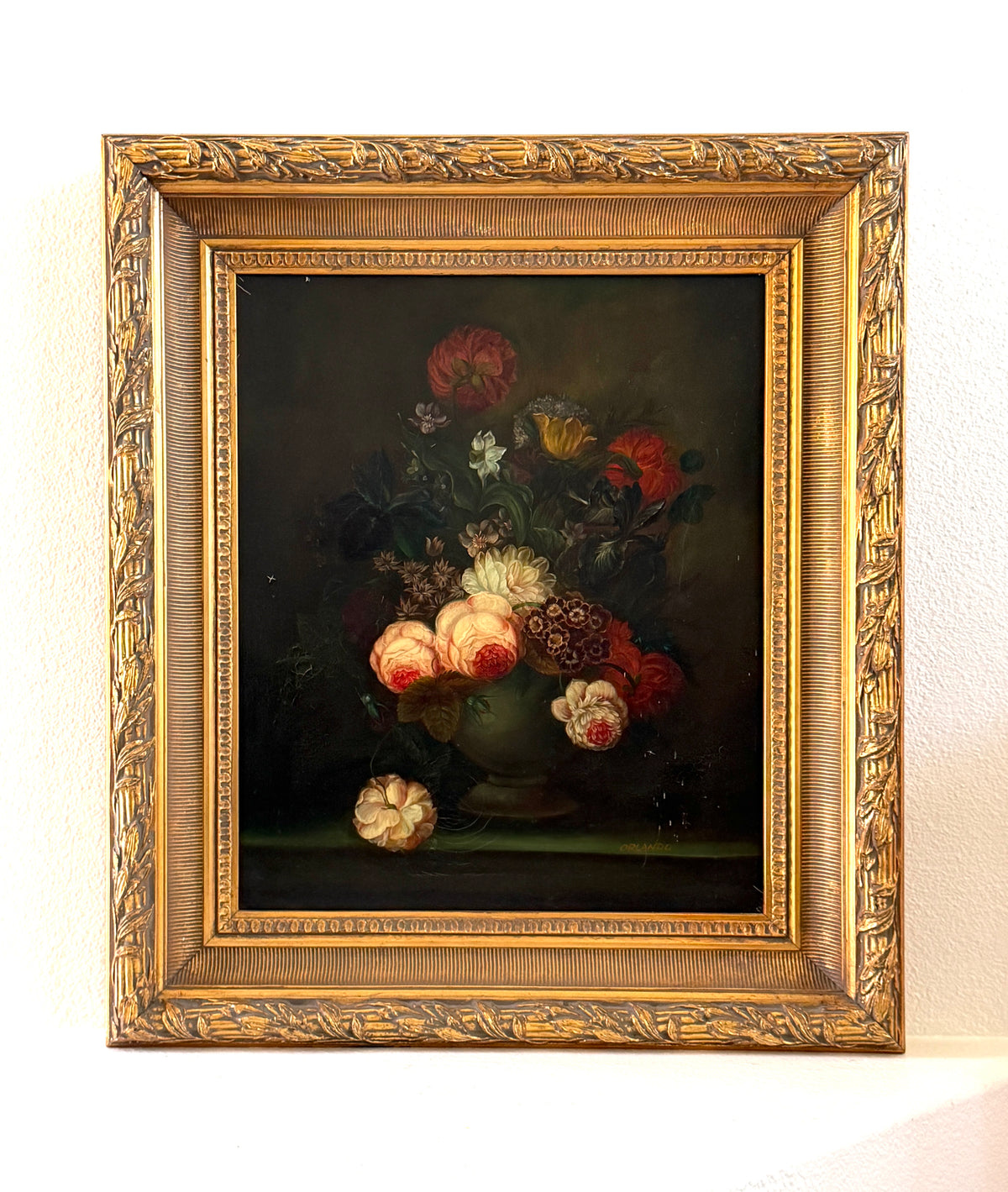 A framed still life painting featuring a bouquet of red, pink, and white flowers in a vase signed Orlando 