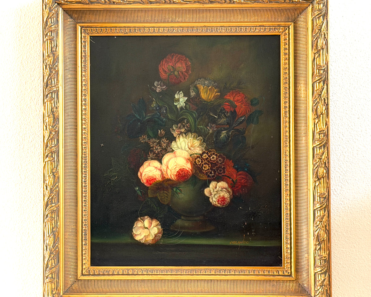 A framed still life oil painting depicting a vibrant bouquet of red, pink, and white flowers in a dark vase against a dark background, housed in an ornate gold frame.