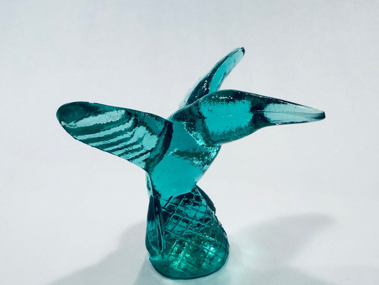 A translucent teal glass sculpture of a hummingbird in flight, featuring a textured body and wings with a matching textured base Made In Italy 