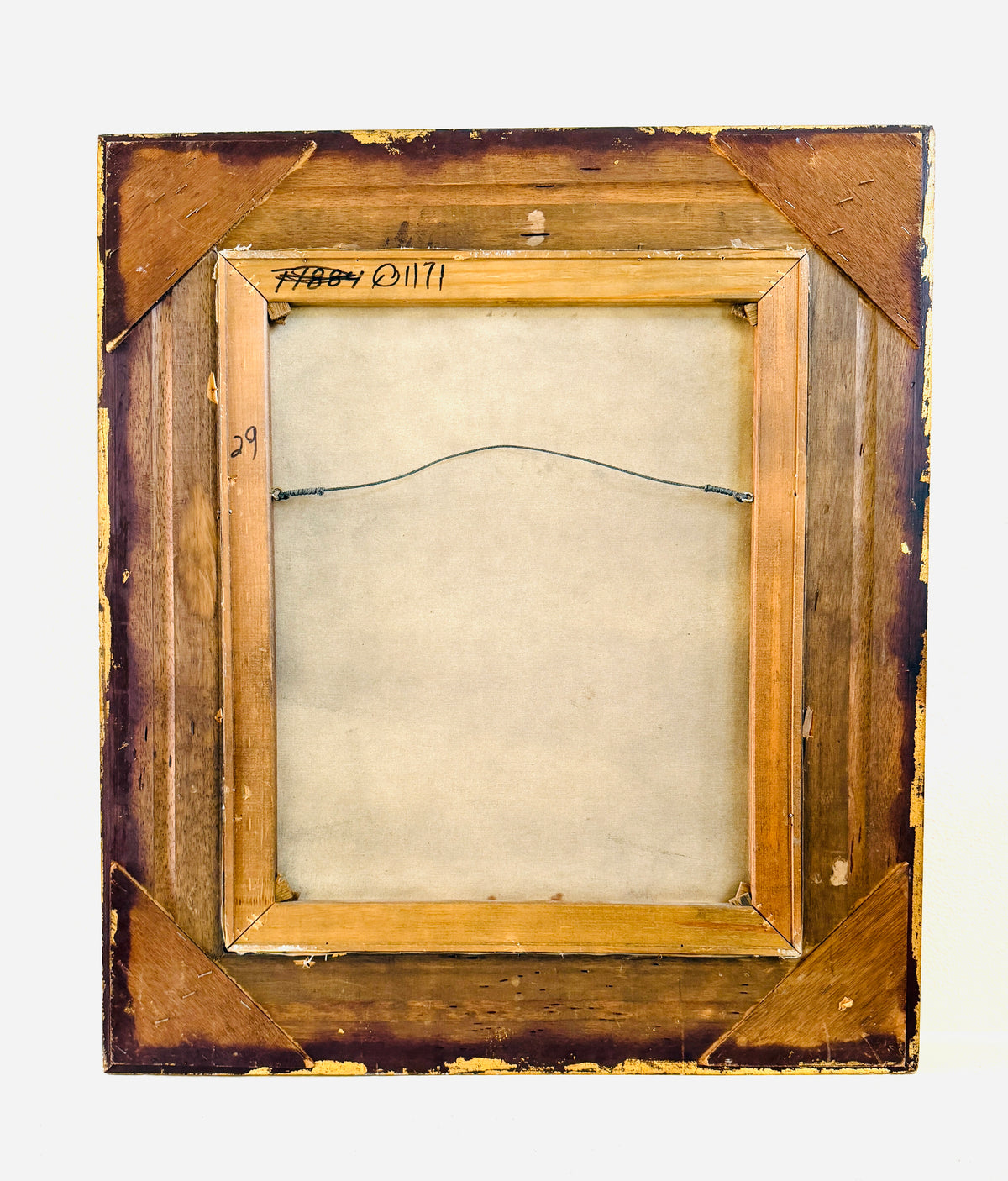 The back of a vintage wooden picture frame, showing the mounting canvas, wire hanger, and hand-written inscription 'FABBY O'1171' on a light gray background.