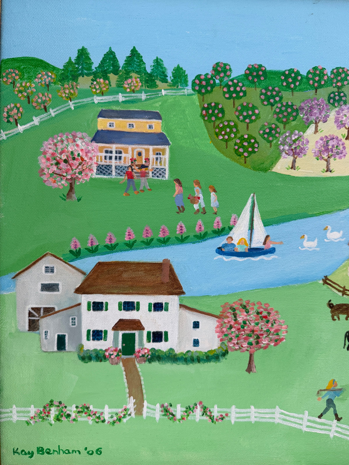A colorful folk-style landscape painting depicting a rural scene with two houses, a blue river, a sailboat, trees, flowers, and small figures of people and animals. The painting is signed 'Kay Berham '06' in the lower left corner.