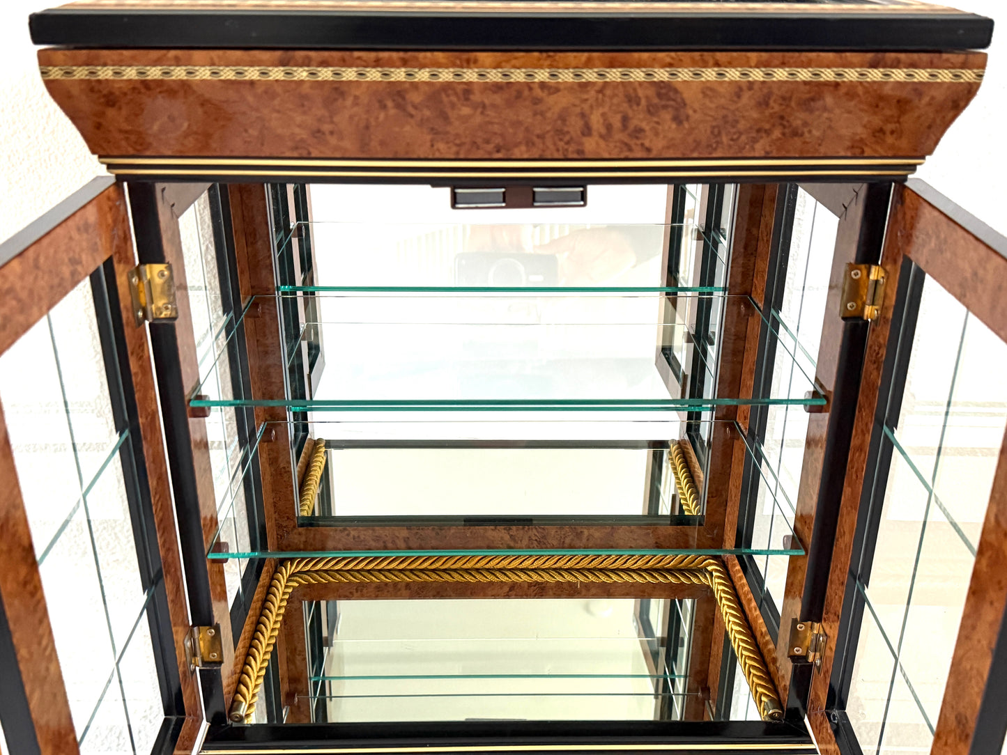 A vintage-style display cabinet with two glass doors, featuring a rich brown burl wood veneer, black trim, gold geometric inlay, and gold tassels on the door handles made in Italy
