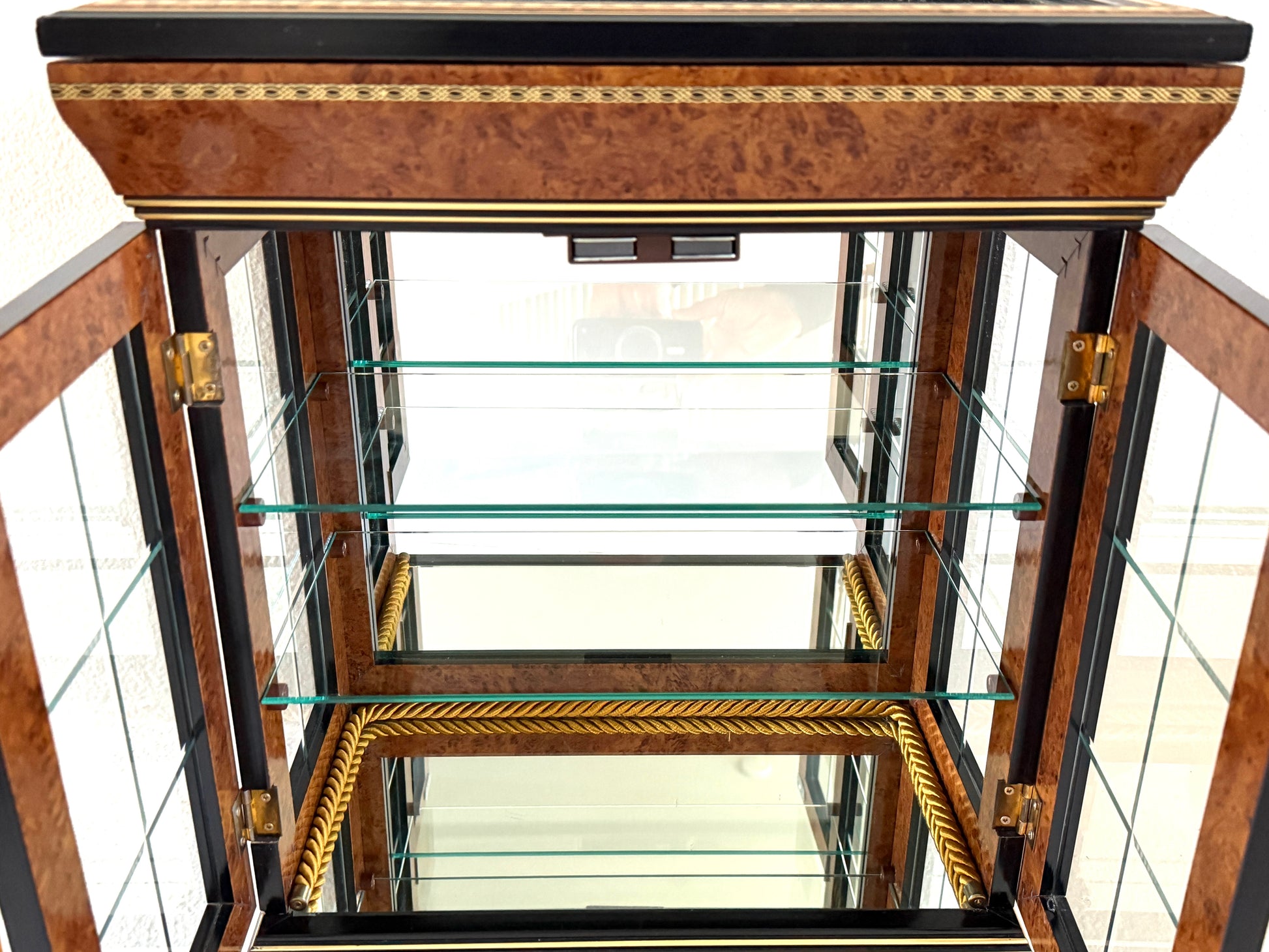 A vintage-style display cabinet with two glass doors, featuring a rich brown burl wood veneer, black trim, gold geometric inlay, and gold tassels on the door handles made in Italy