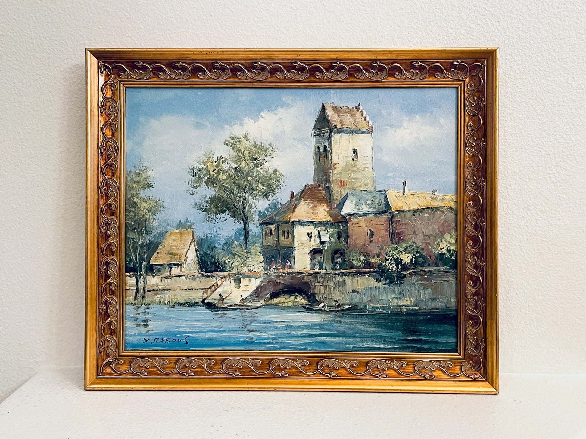 X Rabous Signed Framed painting of a village by a river with ornate gold frame.