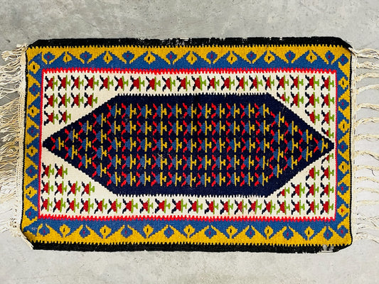 A vintage Kurdish handwoven geometric kilim rug with a colorful border in red, green, white, blue, and yellow, and a central figurative design in a darker color.