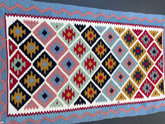 A colorful, geometric-patterned Shiraz Persian kilim rug with a vintage artistic design, featuring diamond shapes and tribal textures, laid out on a flat surface.