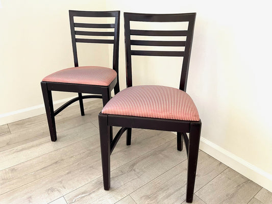 A pair of mid century modern upholstered accent chairs with dark brown wood frames and pink striped silk upholstery.
