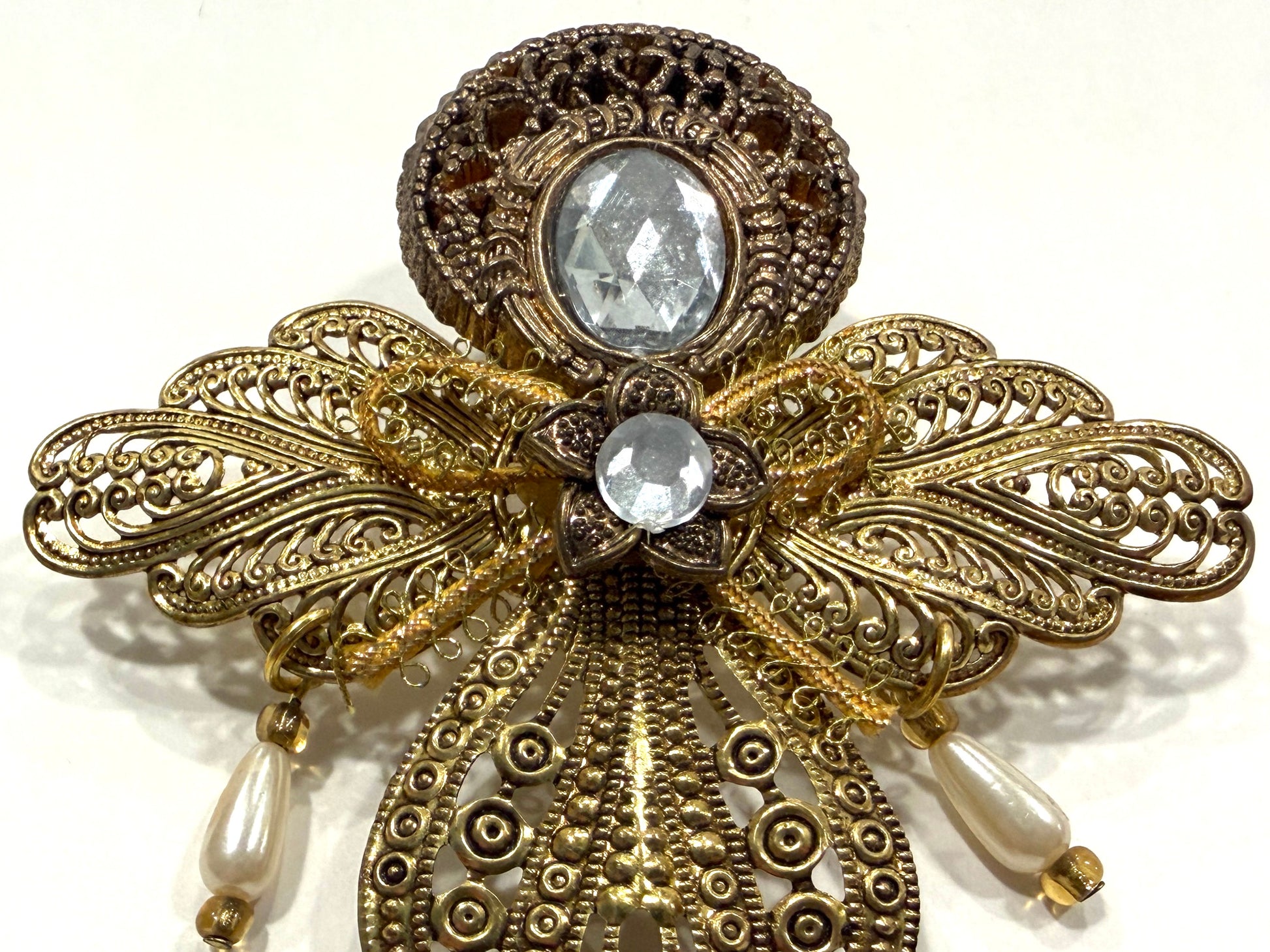 Decorative brooch with gold filigree, pearls, and clear gemstones on a white background