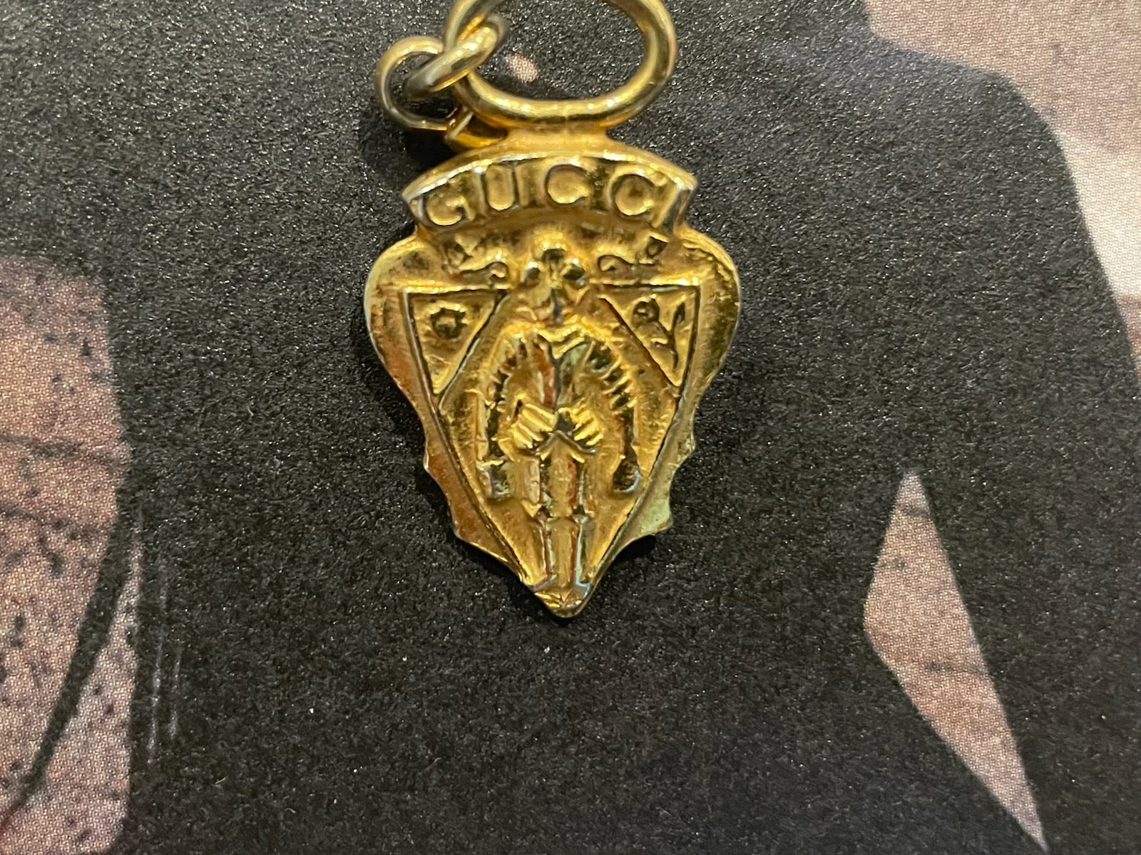 Gold pendant with 'Gucci' branding on a dark background