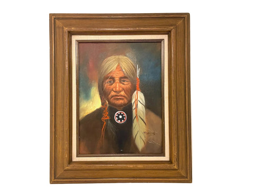 A framed oil portrait painting of a Native American chief with a feather and medallion on display, signed by Morando, with a white linen liner.