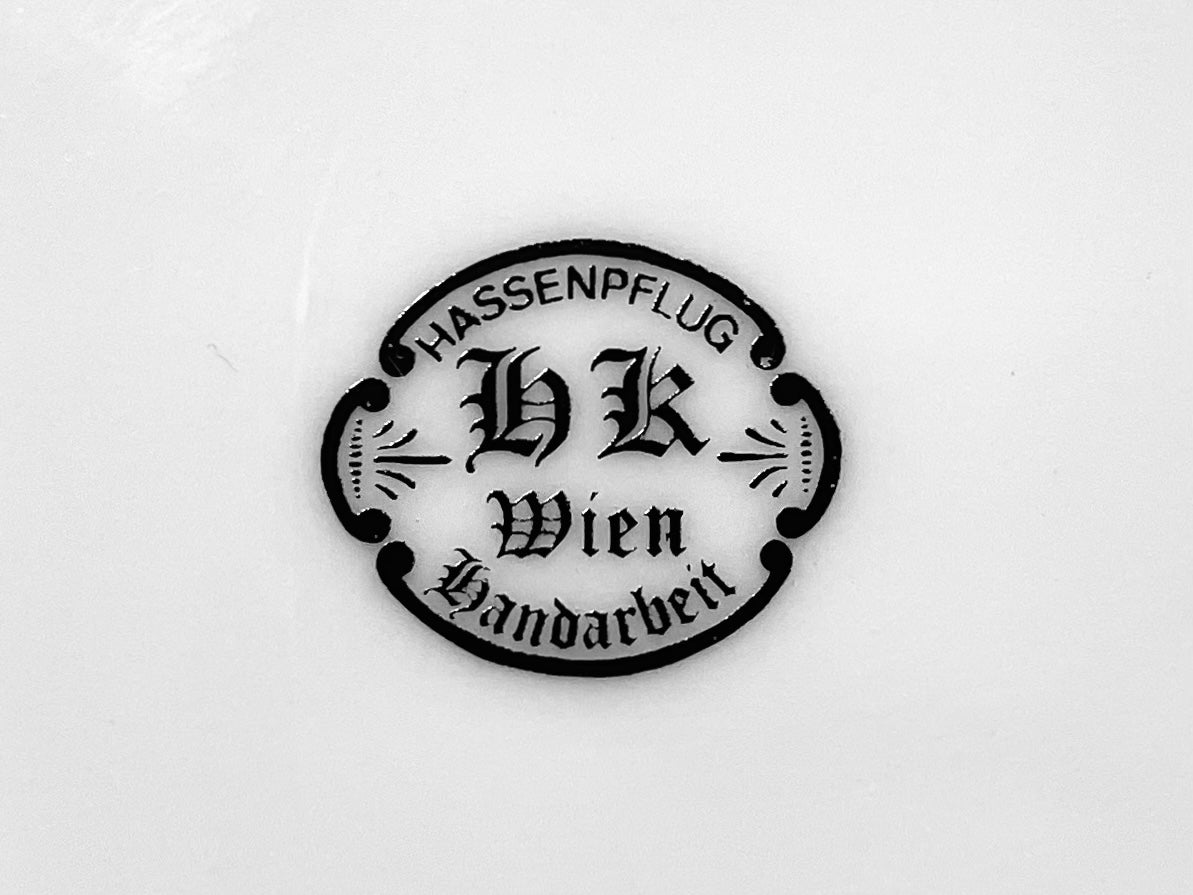 Circular logo with text 'Hassenpflug HK Wien Handarbeit' on a white background